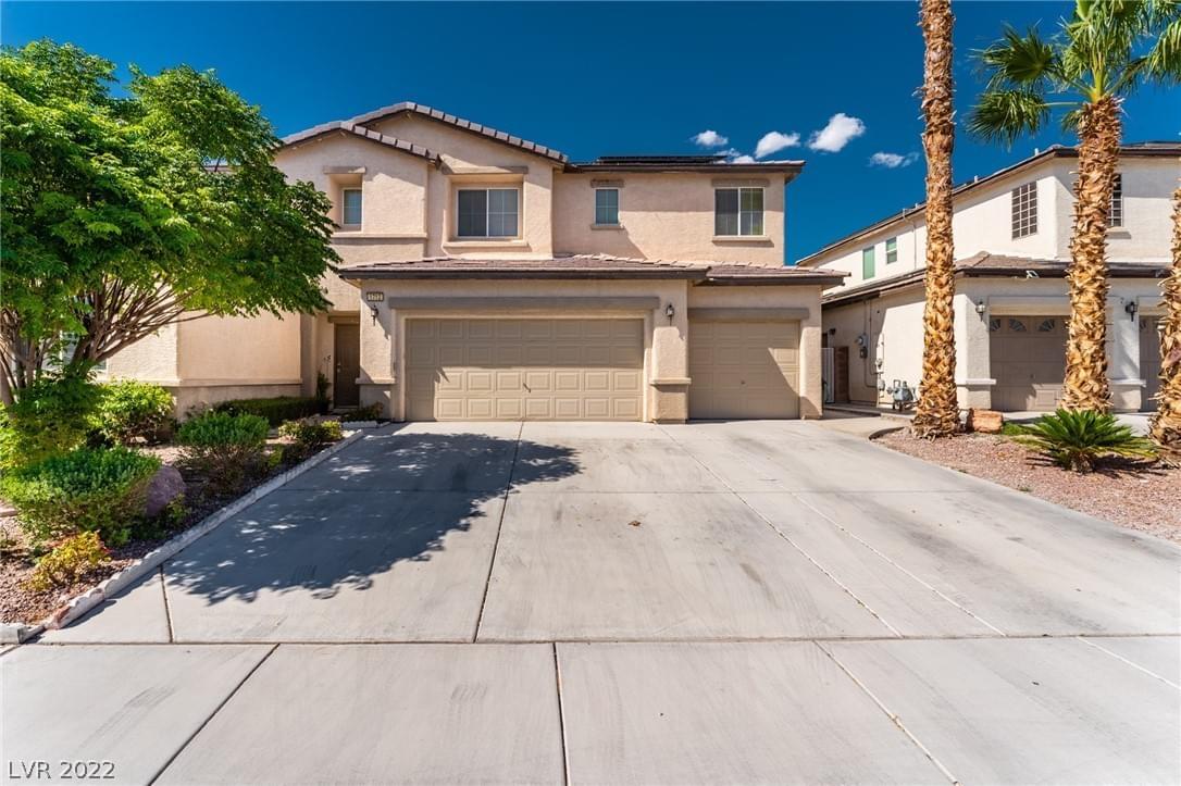 A light brown stucco home with large garage, palm trees and green landscaping, concrete front drive